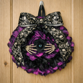 Purple and black circular striped wreath with an eye at the middle and two skeleton hands spreading the flower to see out and a lovely victorian bow at the top
